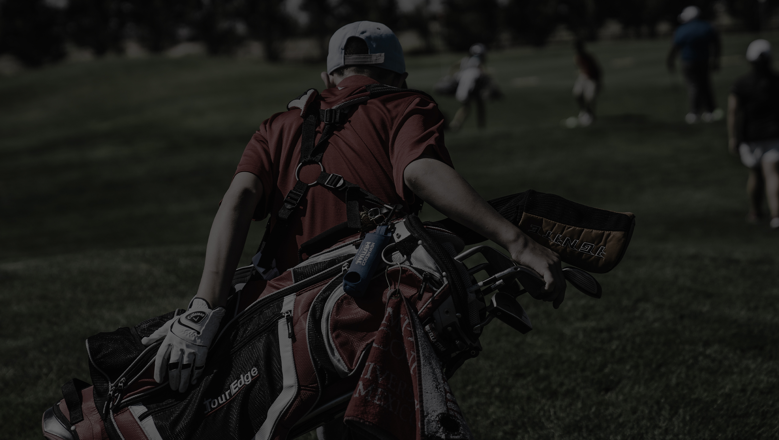 Caddie carrying heavy golf bag on fairway with other golfers