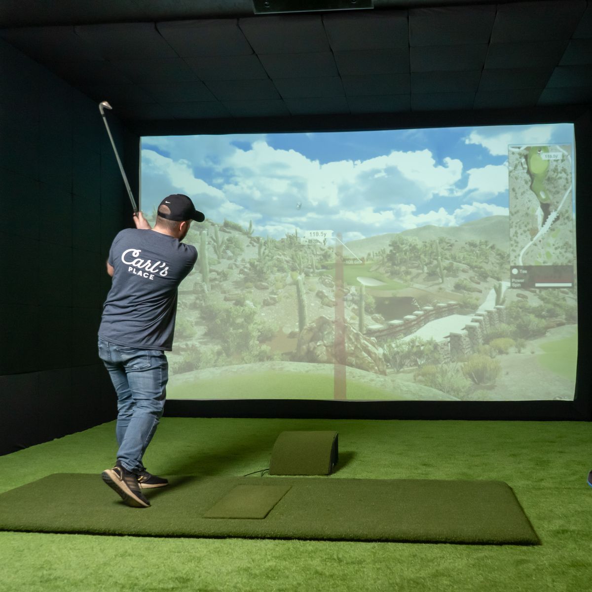 Golfer in golf simulator with enclosure to protect projector on floor